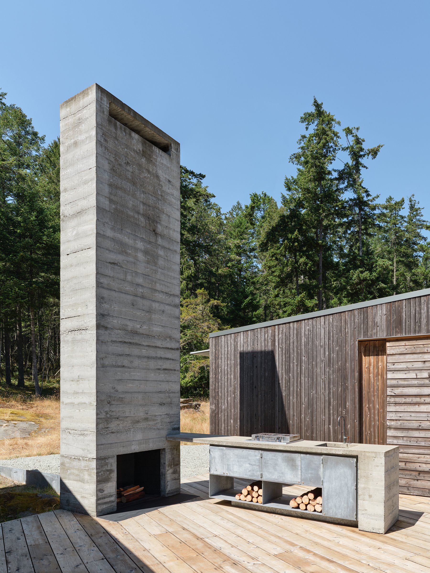 Board-formed concrete fireplace anchoring the Cabin 1+1 open-air kitchen on Galiano Island