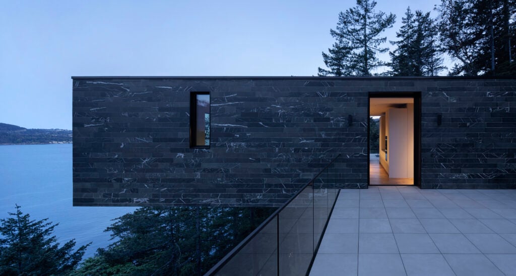 Exterior side view of the home's cantilevered upper level with a glimpse of the side deck with glass railing