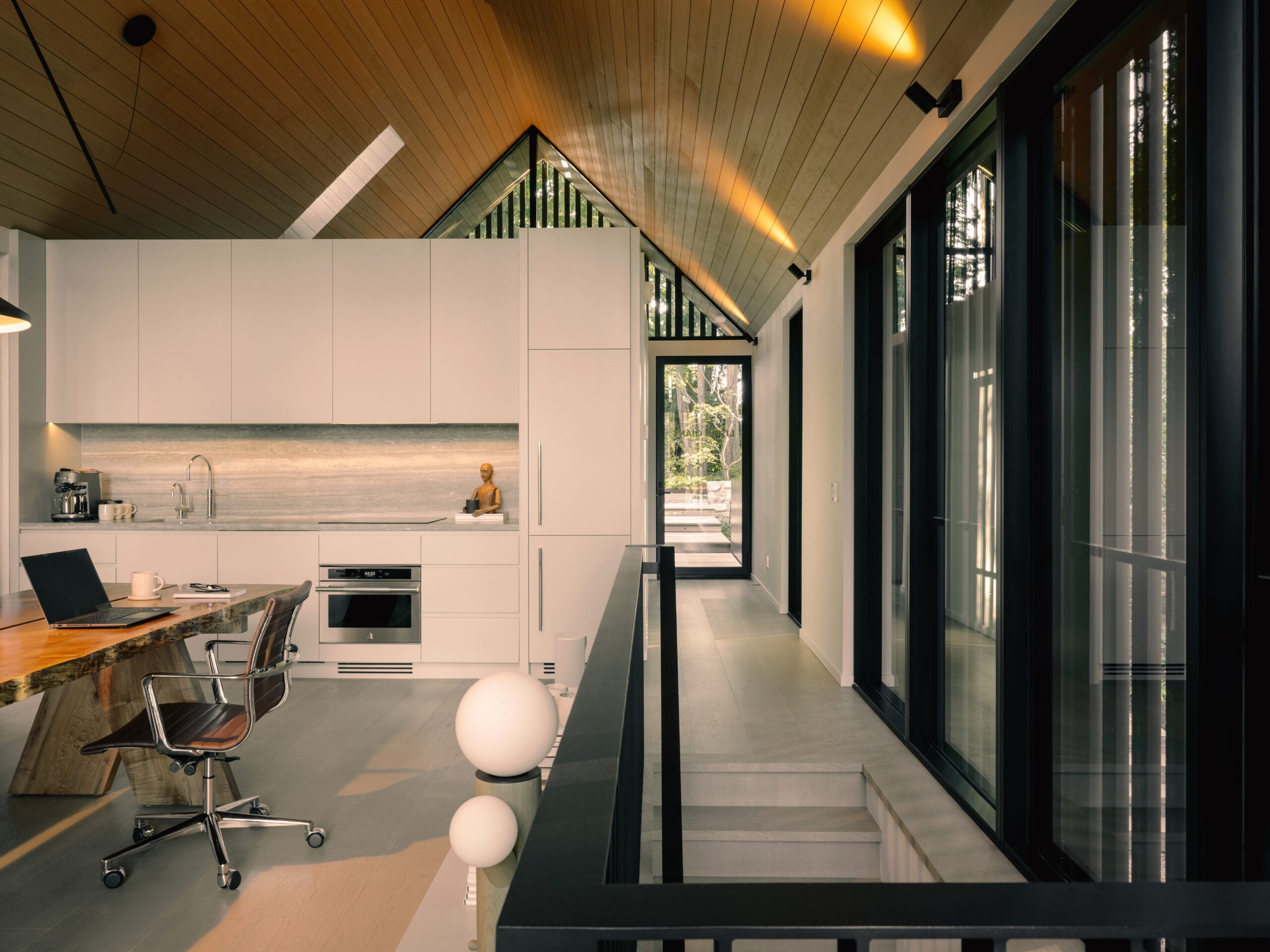 upper-level workspace with white kitchen cabinets, hardwood flooring and large wood table under a vaulted ceiling