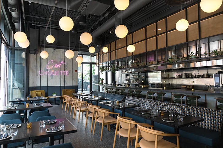 Bar Chouette interior: Chic restaurant dining area with pendant lights, wooden chairs and a neon 'C'est Chouette' sign on the wall.