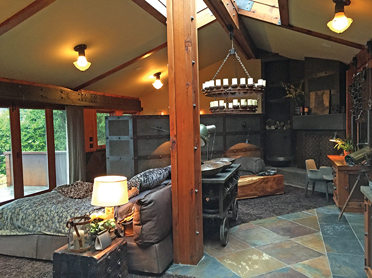 Before image of bedroom with wooden beams and a chandelier, featuring a brown bed and warm lighting.