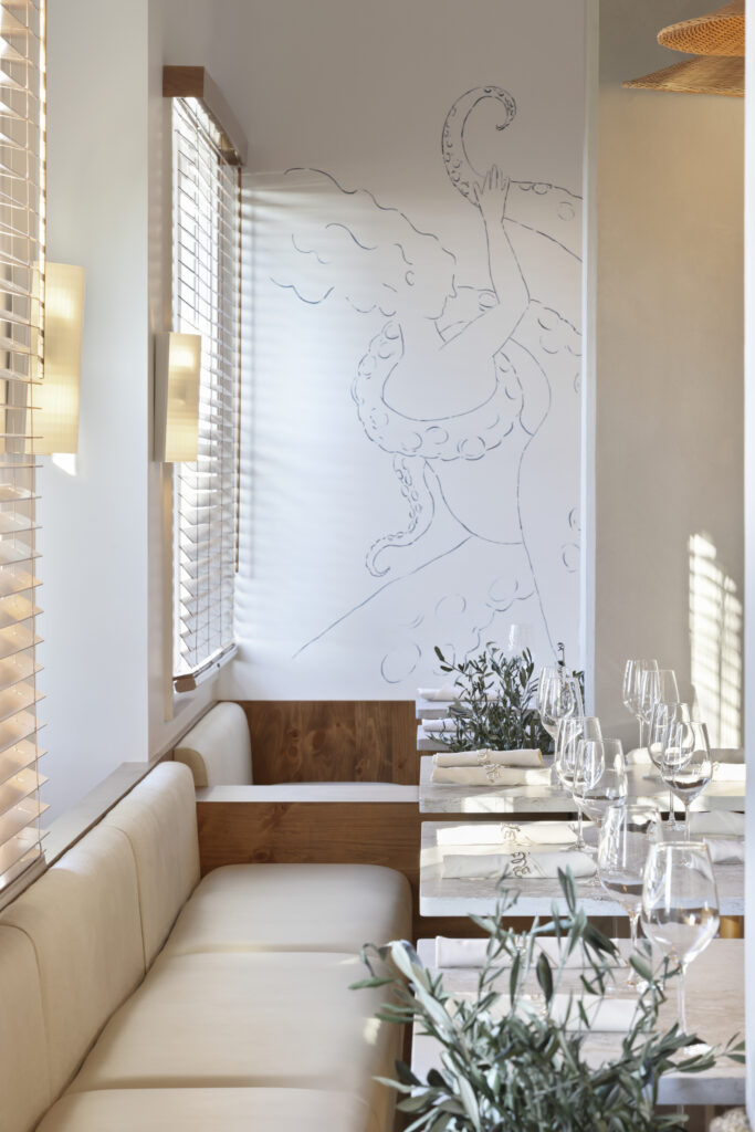 Banquette seating in cream upholstery with a mural of a woman holding an octopus tentacle