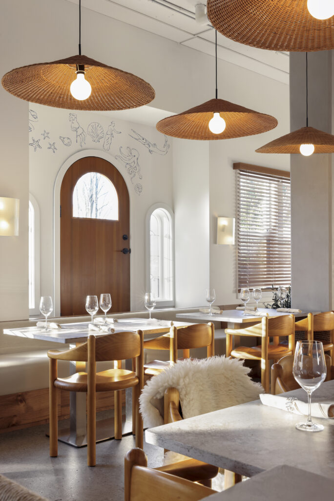 Dining space with pine chairs, quartz tables, rattan pendant lights, and a wood arched door framed by arched windows and wall murals