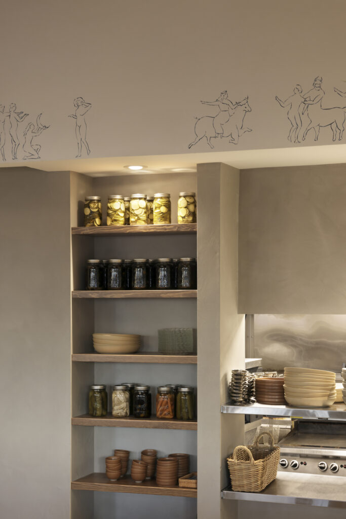 Open shelving with jars and ceramics, with drawings of Greek-style figures along the bulkhead