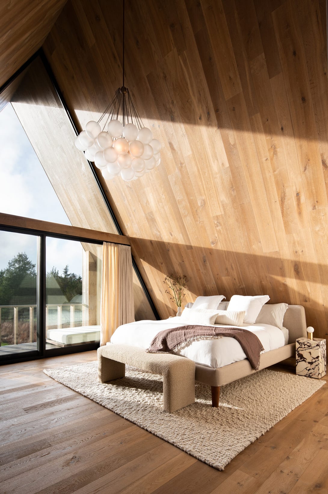 Airy bedroom with warm European oak flooring, wood-clad walls and ceiling, and large windows