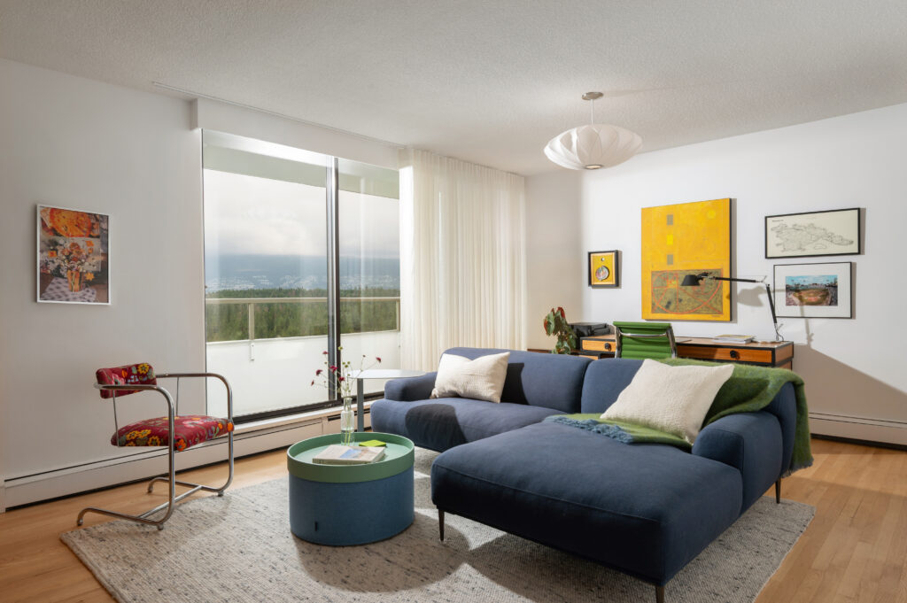 Apartment living room view with blue sectional, coffee table, red vintage chair and vintage wood desk