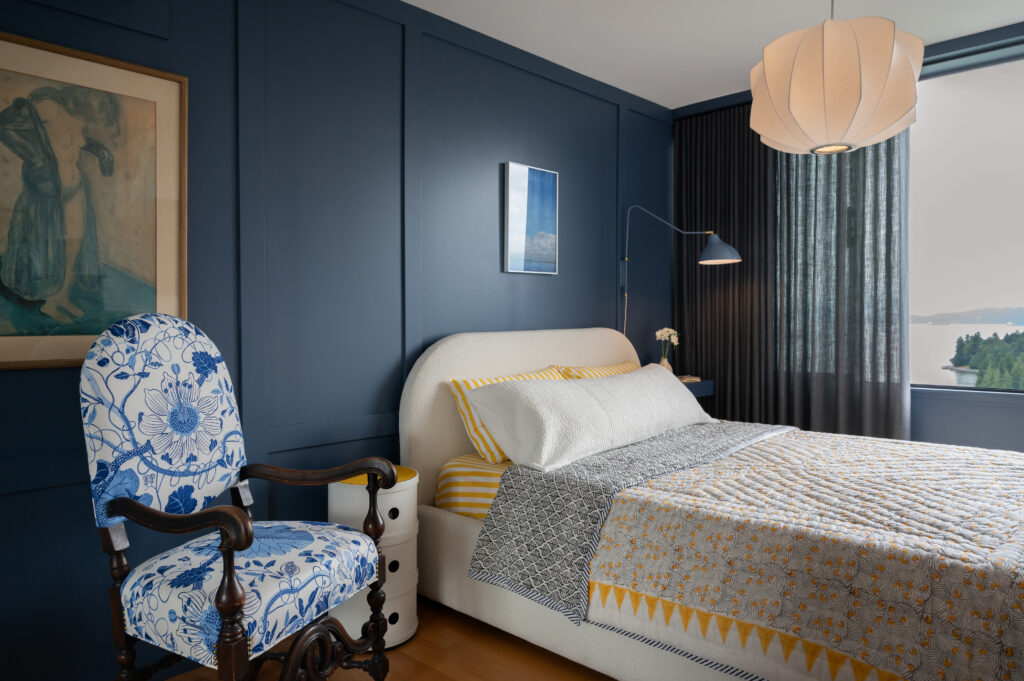 apartment bedroom view with blue painted walls, wall moulding, patterned bedding, and vintage side chair