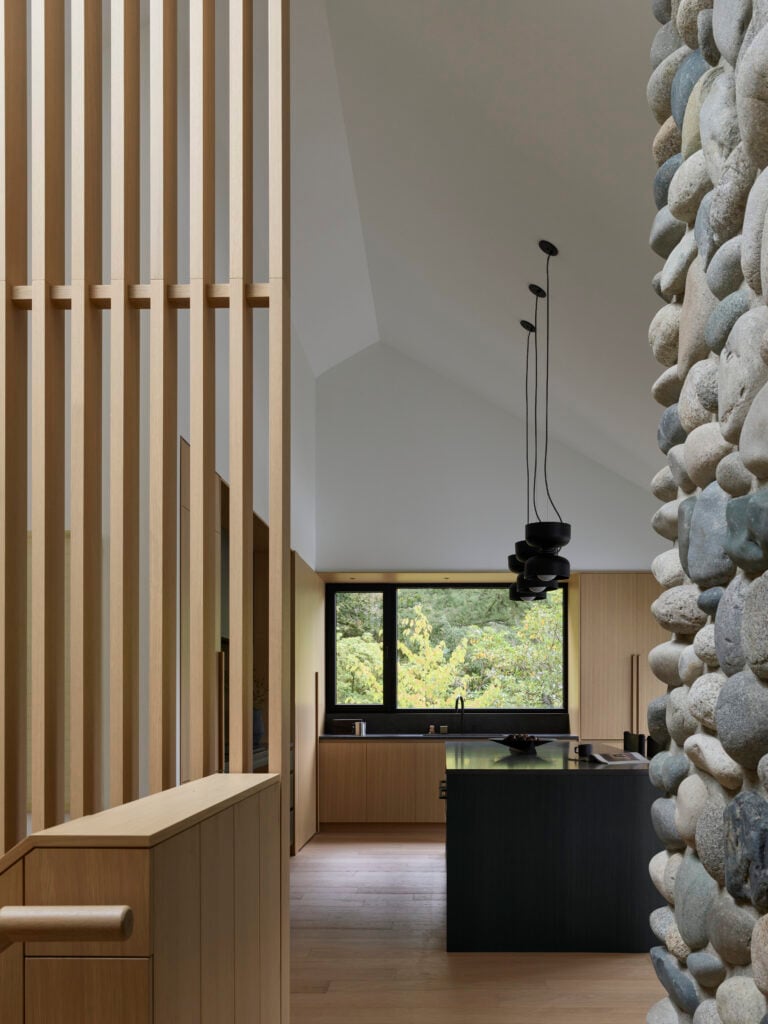 View toward kitchen framed by vertical wooden slats and river rock fireplace
