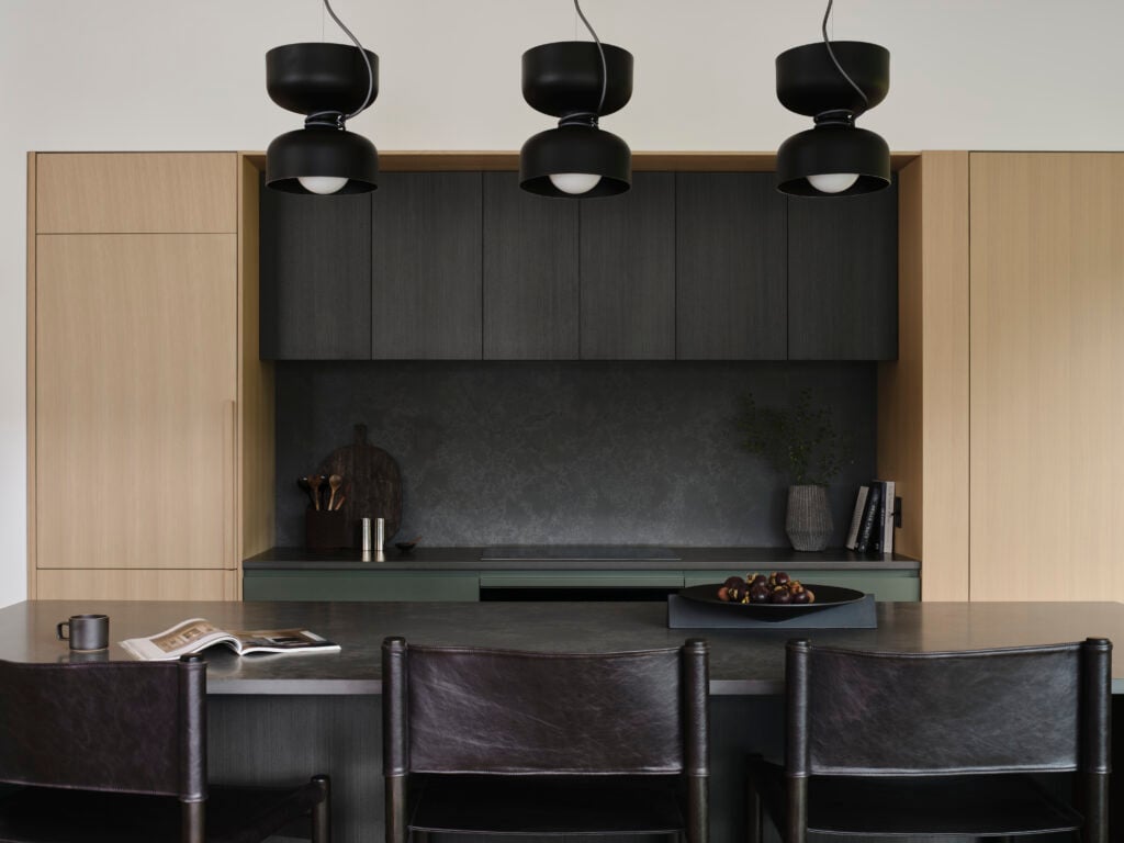 Kitchen with brown black cabinetry, light wood millwork, green drawers and three sculptural pendant lights above a breakfast bar