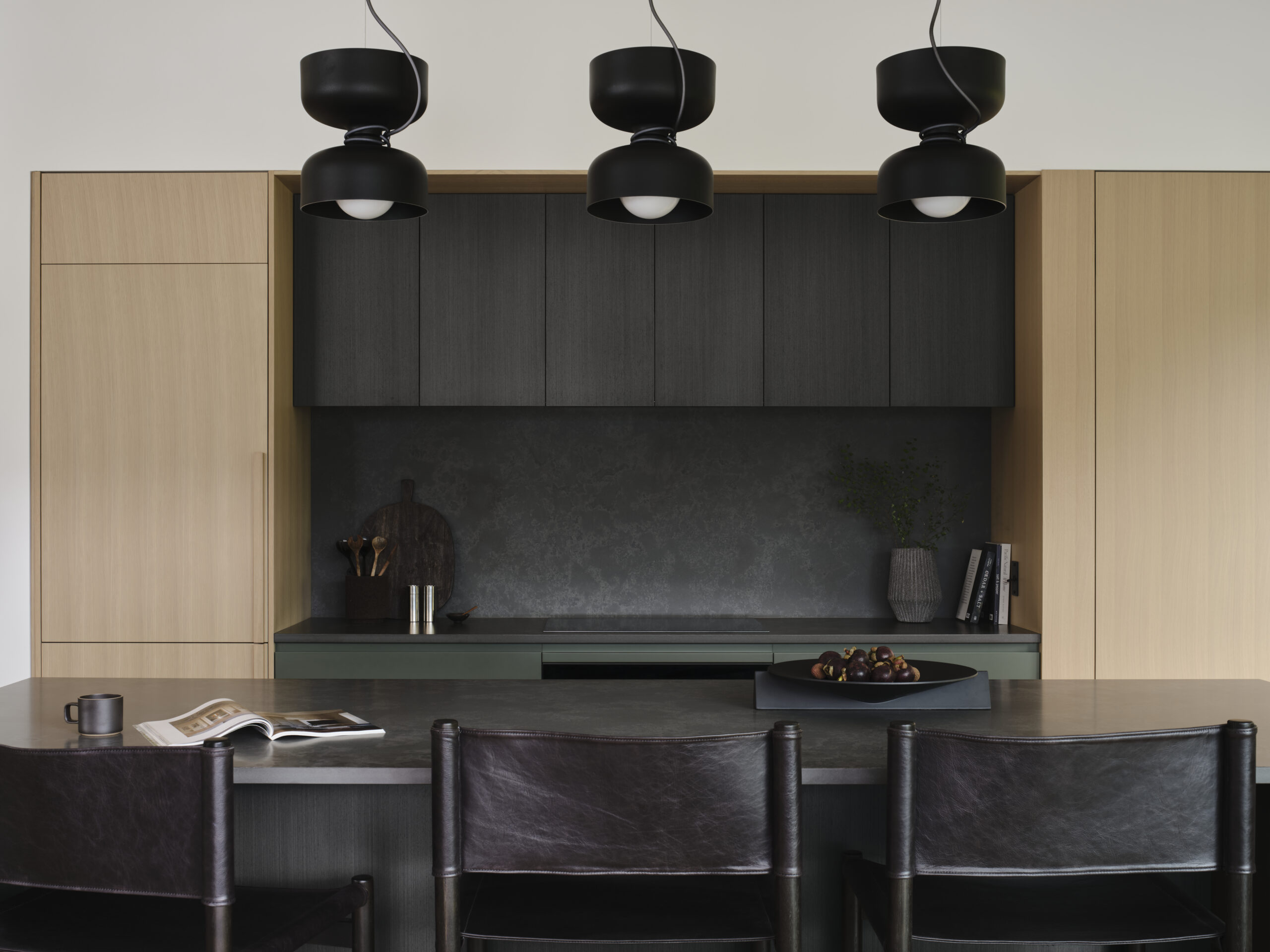 Kitchen with brown black cabinetry, warm wood millwork, green drawers and three sculptural pendant lights above a breakfast bar