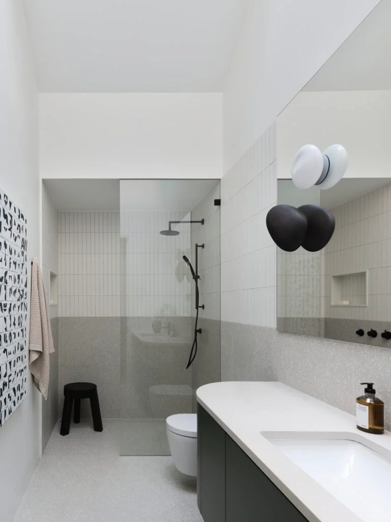 Bathroom with a walk-in shower, dark green vanity and black and white wall sconces