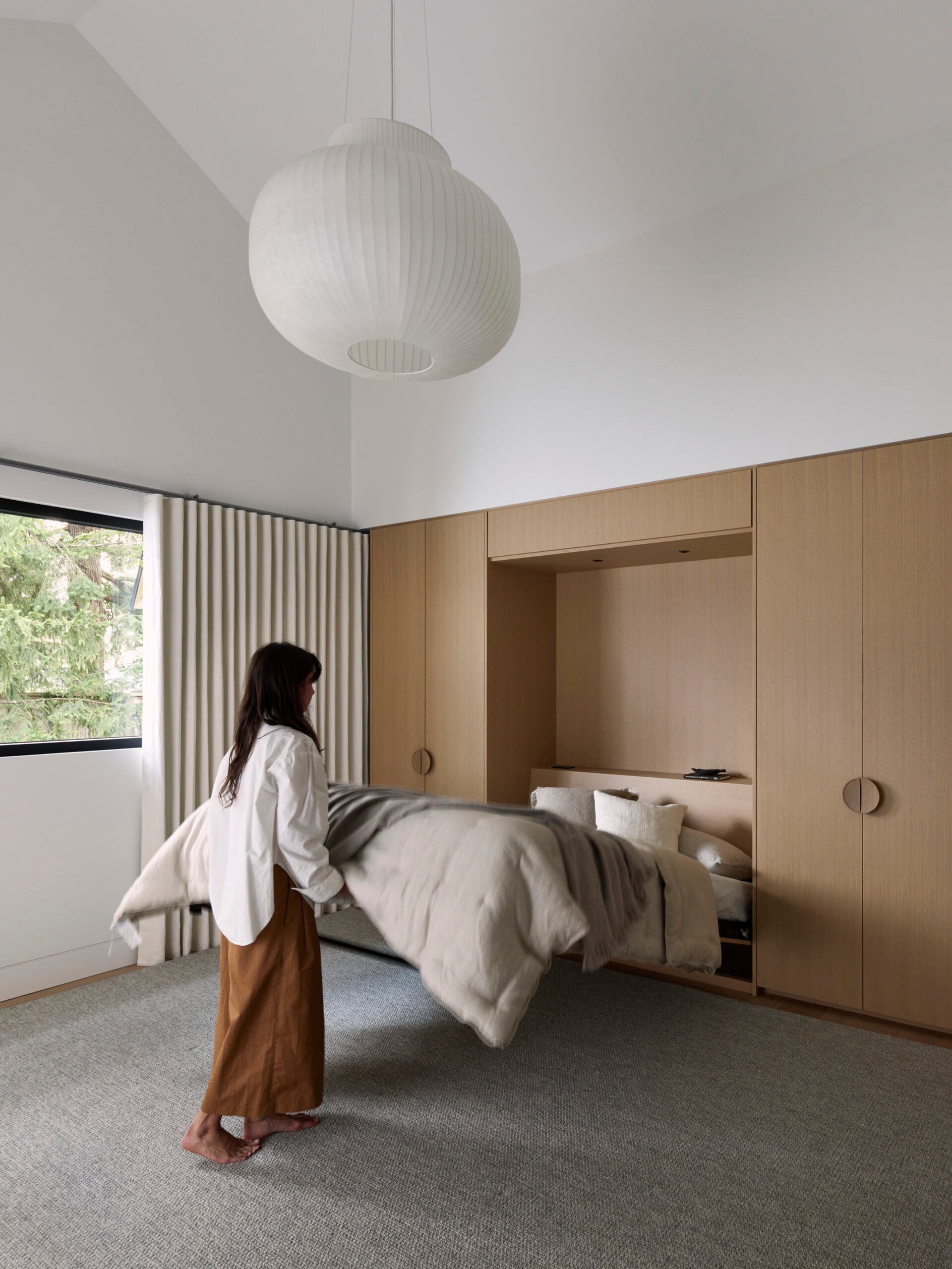A multi-purpose playroom and guest suite with built-in wood cabinetry, a Murphy bed and a sculptural white pendant light.