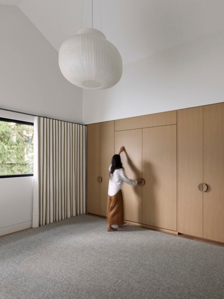 Woman folding up a Murphy bed built into wood cabinetry in a flexible guest suite and playroom