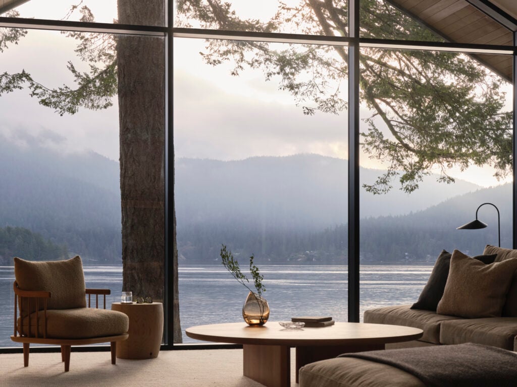Living room with armchair, coffee table, and sectional overlooking the ocean through floor-to-ceiling windows