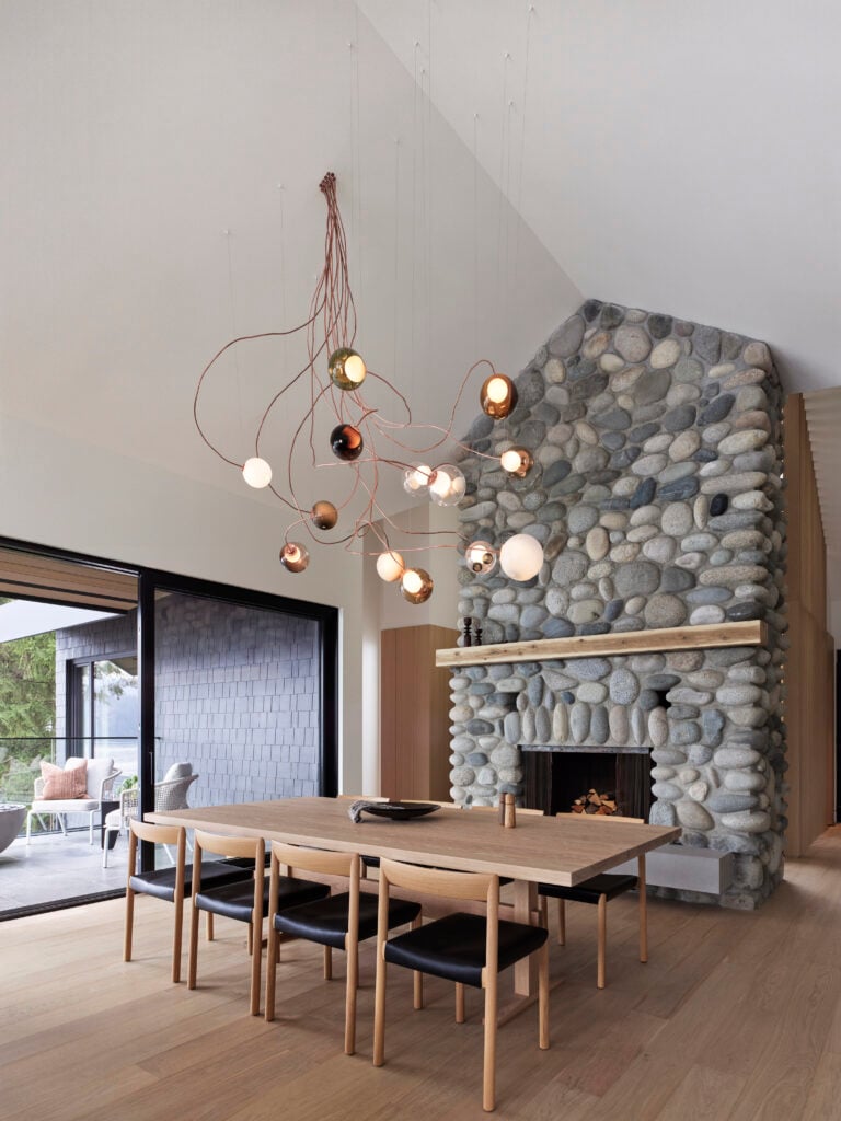 Dining area with a river rock fireplace, vaulted ceiling and Bocci pendant lights above a wood table