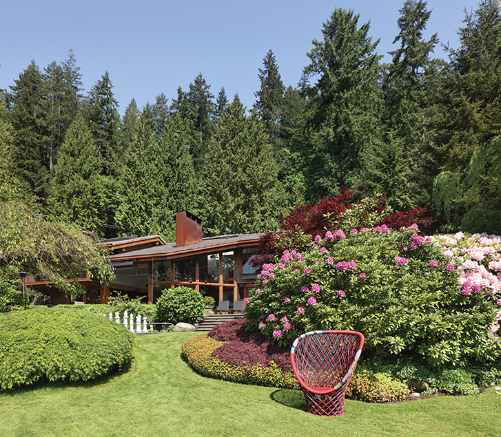 Modern home surrounded by lush greenery and colourful flowers with a red chair on the lawn.