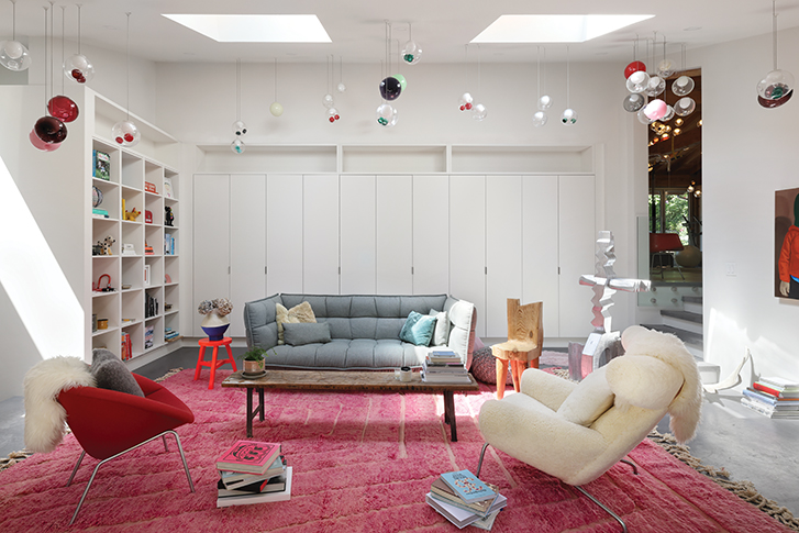 Bright modern living room with a grey sofa, colourful cushions and two armchairs on a pink rug, featuring hanging pendant lights.