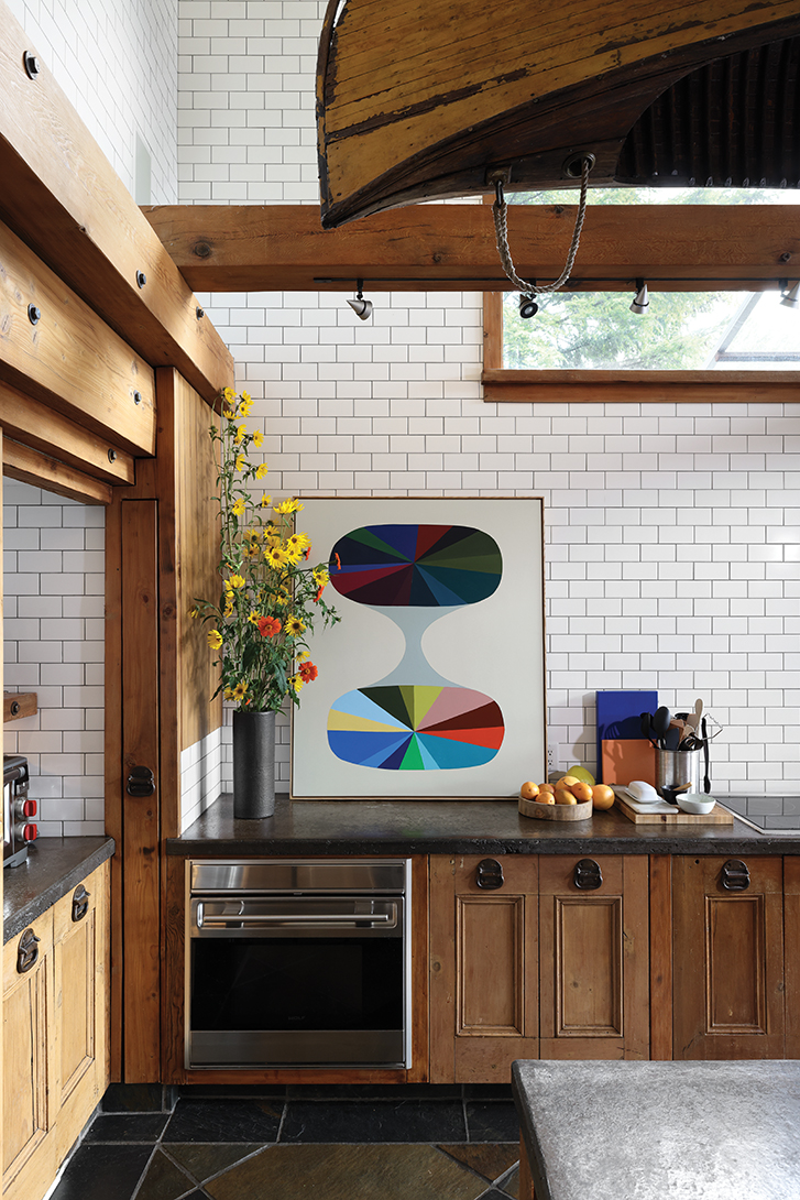 Kitchen with wooden cabinets, white subway tile backsplash, and colourful artwork on the counter.