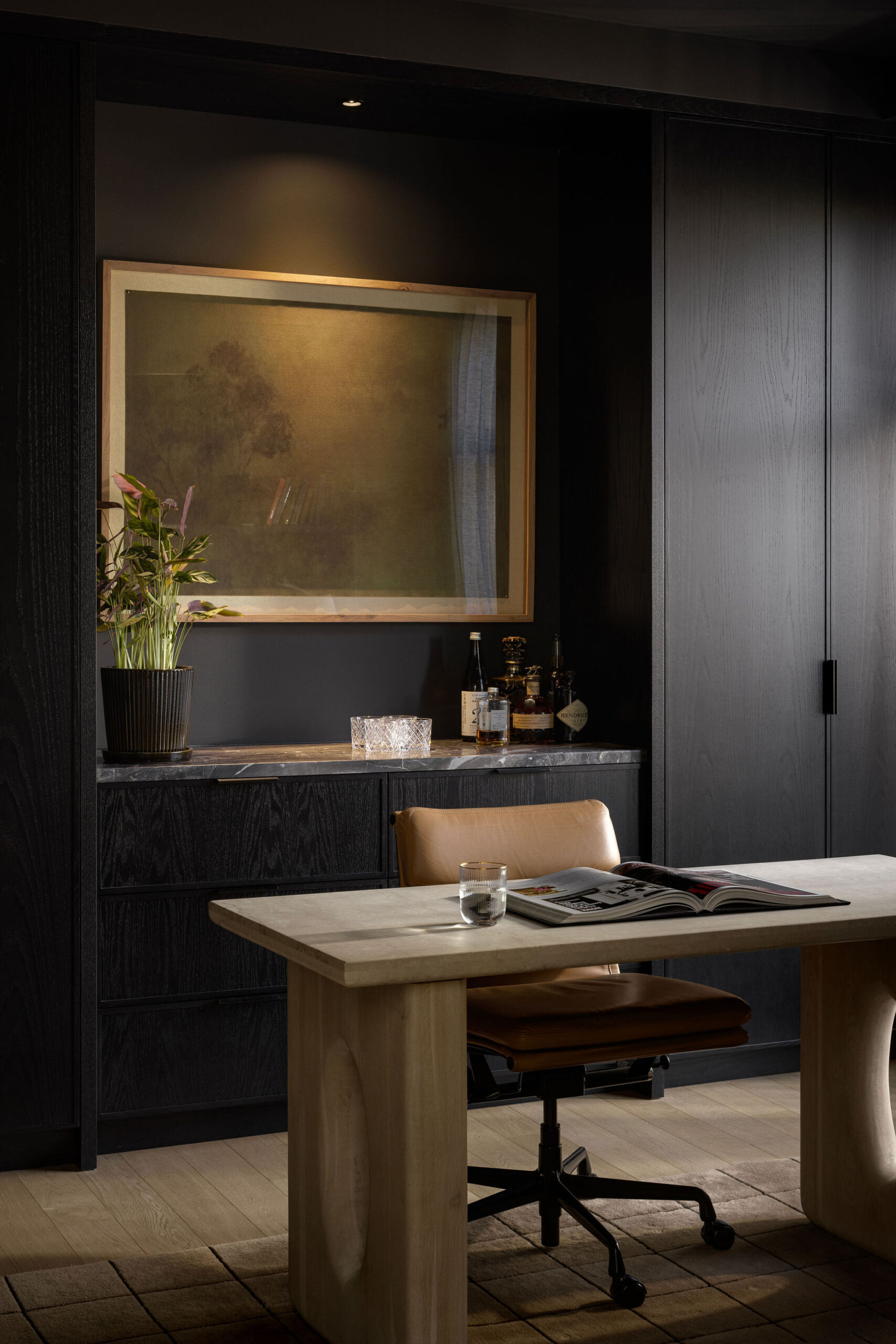Home office with desk, dark cabinetry, wine bar and framed artwork above