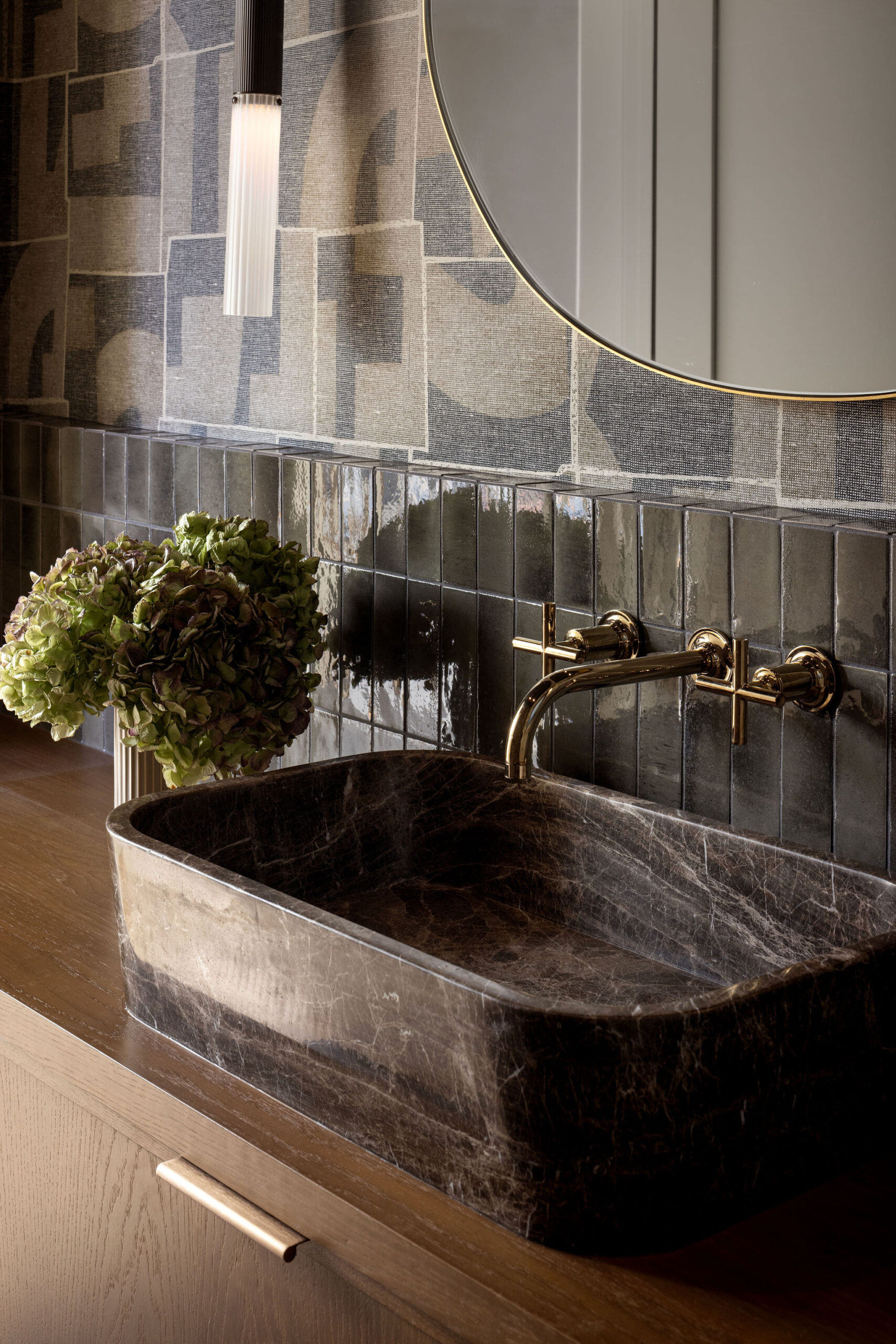 Powder room with carved stone basin sink, brass fixtures, wall tile and patterned wallpaper