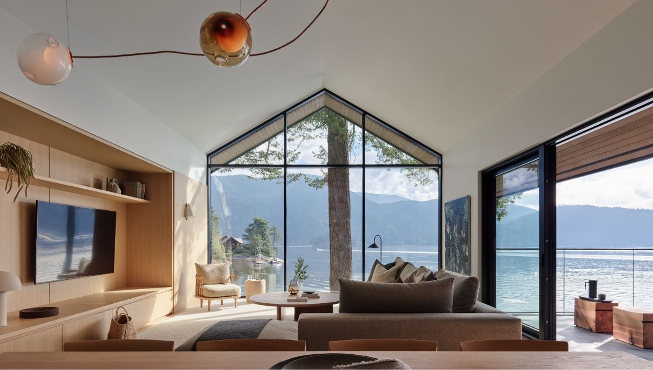 Interior view of living room with vaulted ceilings, floor-to-ceiling windows, neutral and wood furnishings, and ocean view.