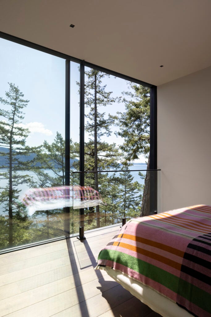 Bedroom with striped blanket and floor-to-ceiling glazing showing treetop and ocean views