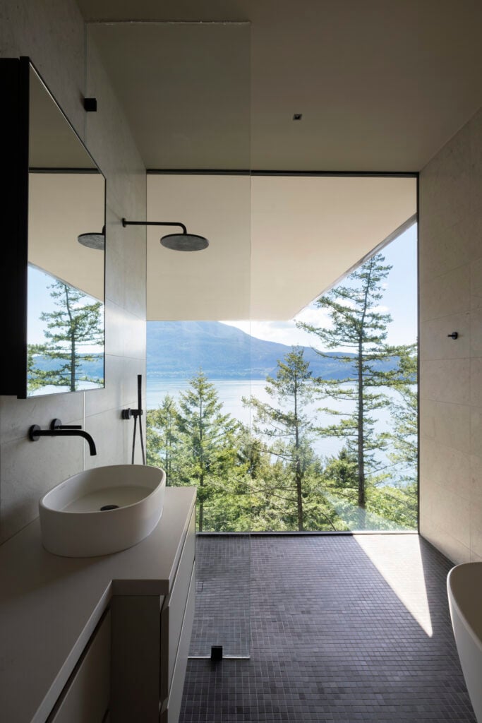 Bathroom with walk-in shower and floor-to-ceiling window with views of treetops, water, and the cantilevered structure above