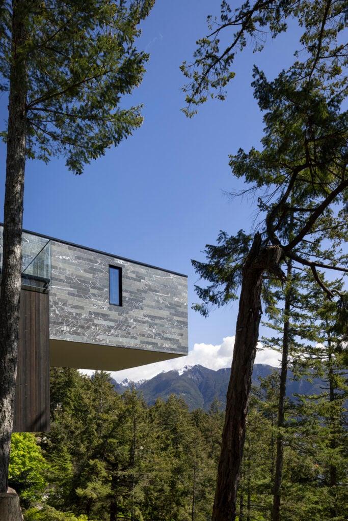 Angled exterior view of the home’s cantilevered upper level with textured slate cladding and forest and mountain views below