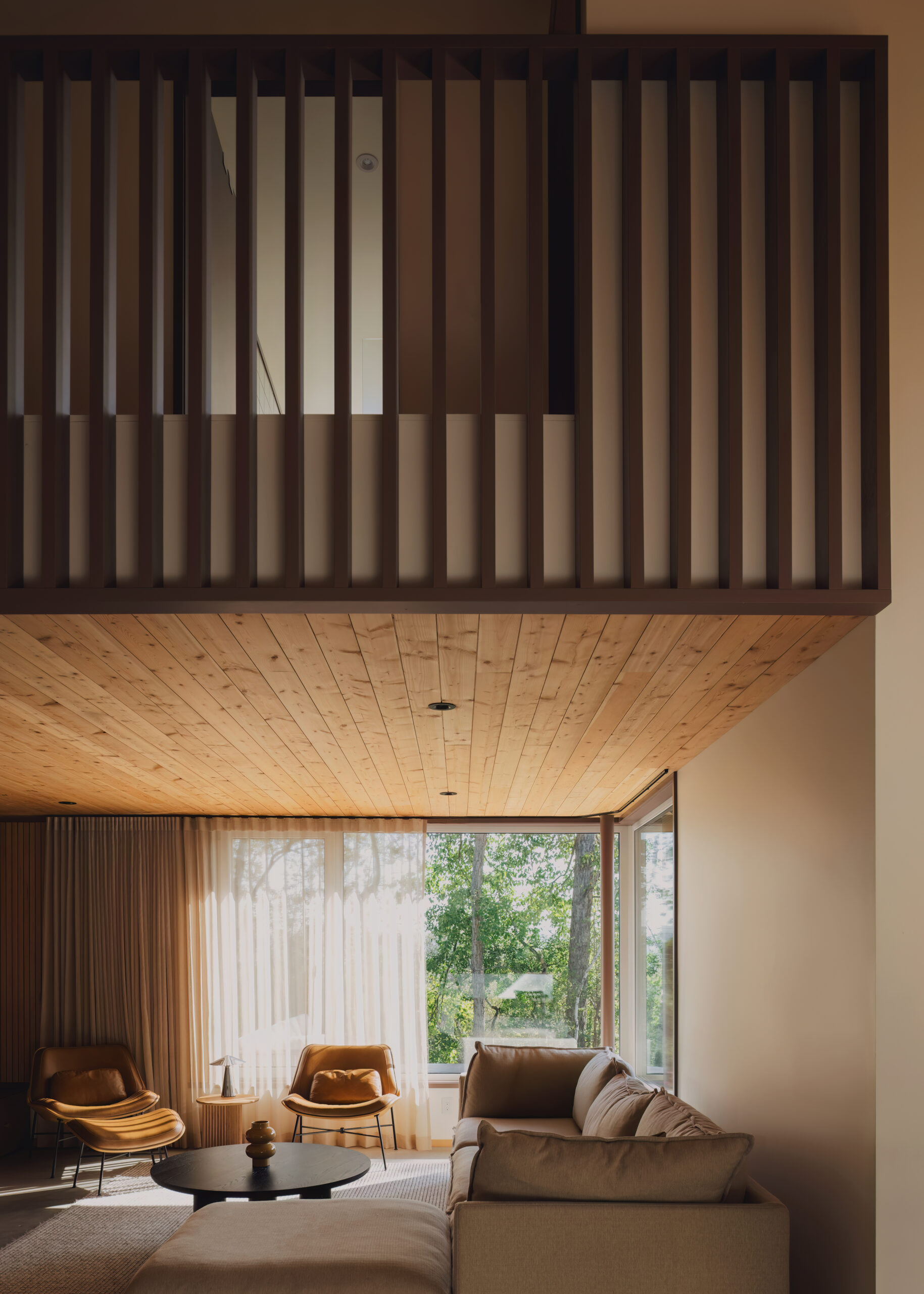 Living room with sofa, leather chairs, wood ceiling and upper floor railing