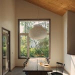 Dining area with long wood table, large window and pendant light